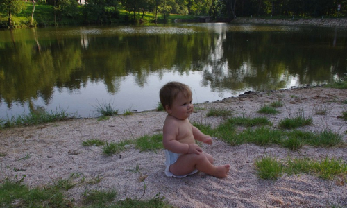 Matěj sed&iacute; na jemn&eacute;m &scaron;těrku na břehu rybn&iacute;ka.